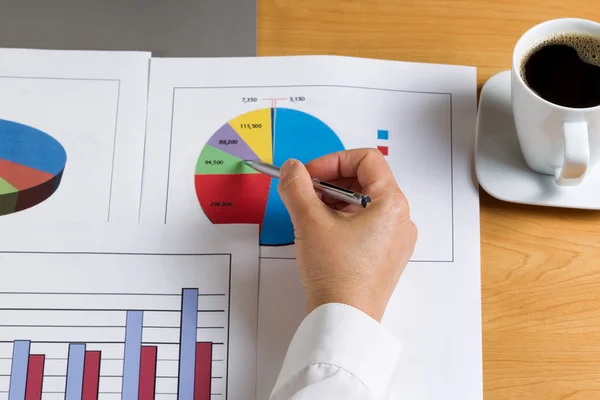 Hand som håller pennan medan du tittar på data finansiella cirkeldiagram — Stockfoto