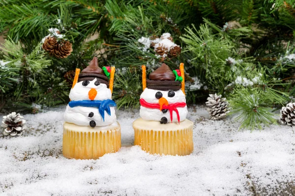 Decorado cupcake muñecos de nieve sobre fondo de hoja perenne nevado — Foto de Stock