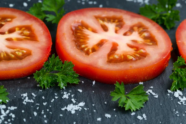 Freshly sliced ripe tomato on black slate stone background — Stock Photo, Image