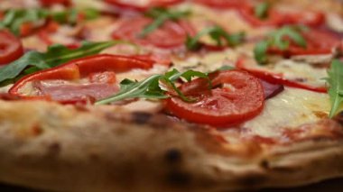 İtalyan pizzası, salamlı, domatesli, kırmızı biberli ve roka ahşap bir masa üzerinde. Jambon, domates, paprika ve roka..