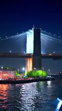 Brooklyn Köprüsü gece East River üzerinde aydınlandı. Iconic Brooklyn Köprüsü, East River 'ın üzerinde geceleri yansıyan ışıklarla parıldıyor..