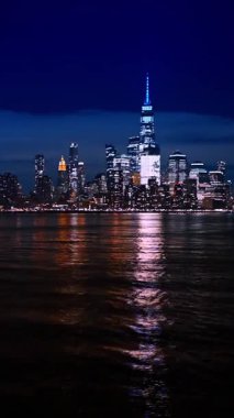 Aşağı Manhattan 'ın gece silueti rıhtımdan. Manhattan 'ın aydınlık gökdelenleri geceleyin Hudson Nehri' ni yansıtıyor..