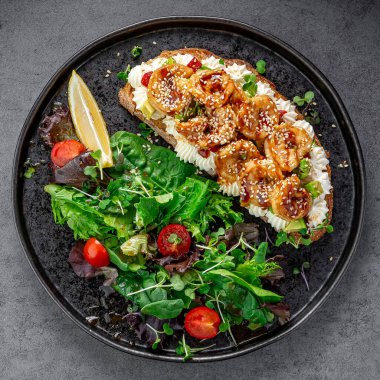 Avokado ve salata soslu karides bruschetta. Avokado, susam, limon ve koyu arkaplanda yeşil salatalı karides bruschetta manzarası..