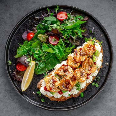 Karides ve salatalı avokado bruschetta. Karides, avokado ve yeşil salata ve limon dilimleriyle servis edilen susam tohumlu bruschetta manzarası..