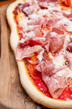 Domates soslu ve parmesanlı jambonlu pizza. İnce dilim jambon, parmesan ve domates soslu İtalyan pizzasının ahşap bir tahtanın üzerindeki detaylı görüntüsü..