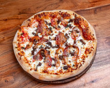 Pastırmalı yuvarlak pizza, mozzarella ve domates sosu. Üstünde pastırma şeritleri, erimiş mozzarella ve ahşap arka planda domates sosu olan sıcak yuvarlak pizza..