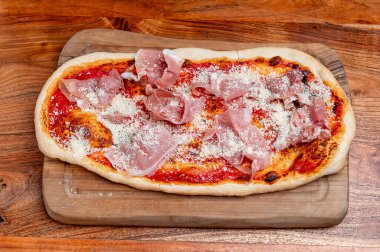 Domates soslu, parmesanlı ve jambonlu kremalı pizza. Köy tahtasında servis edilen domates tabanlı, parmesanlı ve jambonlu düz ekmekli pizza..