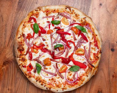 Fesleğen, mozarella, domates ve soğanlı ev yapımı pizza. Mozarella, kırmızı soğan, fesleğen yaprağı ve ahşap masada servis edilen kavrulmuş biberli ev yapımı lezzetli pizza..