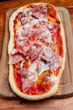 Prosciutto ve parmesan peynirli dikdörtgen İtalyan pizzası. Geleneksel dikdörtgen pizza üzerine domates sosu, prosciutto dilimleri ve sade ahşap bir tahta üzerinde parmesan peyniri..