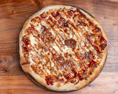 Karamelli soğanlı ve mozarellalı ızgara pizza. Yuvarlak barbekü pizza üzerine sos serpiştirilmiş ve üzeri karamelli soğan ve ahşap arka planda mozzarella peyniri ile kaplı..