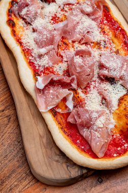 Tahtadaki geleneksel İtalyan jambonlu pizzasına yakın çekim. Yakın plan İtalyan pizzası prosciutto ve parmesan peynirli. Köy tahtasında servis ediliyor..
