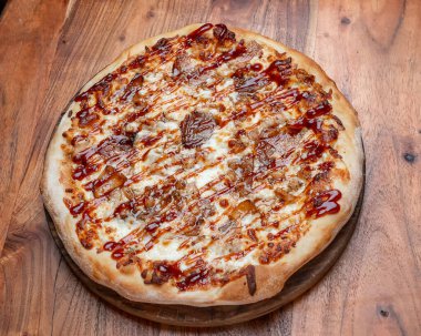 Peynirli, soğanlı ve kahverengi soslu ızgara pizza. Barbekü soslu sıcak yuvarlak pizza, peynir ve ahşap bir masada karamelize soğan..