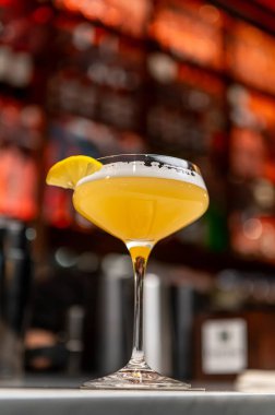 Bar tezgahında limon garnitürlü Citrus kokteyli. Citrus aromalı kokteyl sıcak ortam aydınlatmalı şık bir barda coupe bardakta limon garnitürle servis edilir..