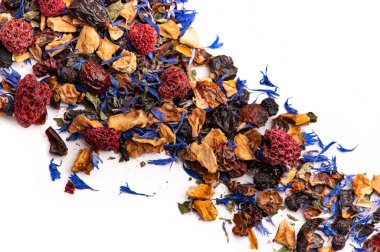 Kurumuş meyveli bitki çayı ve yüzeye saçılmış çiçekler. Kurumuş meyveli bitki çayı, ahududu ve çiçek yaprakları beyaz arka planda dizilmiş..