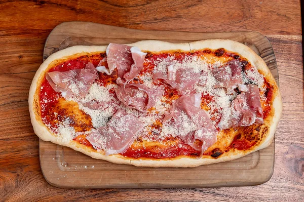 İtalyan pizzası, jambonlu ve parmesanlı. Domates soslu dikdörtgen İtalyan pizzası, jambon dilimleri ve ahşap tahtada rendelenmiş parmesan peyniri..