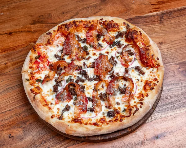 Pastırmalı yuvarlak pizza, mozzarella ve domates sosu. Üstünde pastırma şeritleri, erimiş mozzarella ve ahşap arka planda domates sosu olan sıcak yuvarlak pizza..