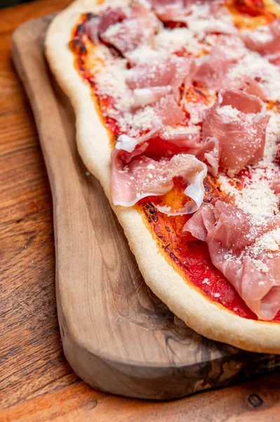 İtalyan usulü, jambonlu ve parmesanlı pizza. Prosciutto, parmesan ve domates soslu geleneksel İtalyan düz ekmek pizzası ahşap bir tahtada servis edilir..