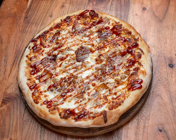 Peynirli, soğanlı ve kahverengi soslu ızgara pizza. Barbekü soslu sıcak yuvarlak pizza, peynir ve ahşap bir masada karamelize soğan..