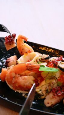 Siyah tabakta çatalla deniz ürünleri servis ediyorum. El, restoranda karides ve ahtapot balığı servis etmek için çatal kullanır..