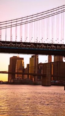 Manhattan sularının üzerindeki asma köprü. New York asma köprüsünün kabloları, sıcak ışık kulesiyle nehir boyunca uzanıyor..