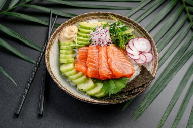 Dilimlenmiş salatalık ve soslu somon balığı kasesi. Taze somon, avokado, salatalık, yosun ve turplu renkli bir somon kabı yanında krema sosu ile sunulur..