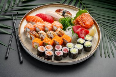 Variety Platter of Sushi, Sashimi, ve Maki Rolls. Dairesel tabakta bol miktarda nigiri, sashimi ve maki dürümleri, gösterişli ton balığı, somon, yılan balığı ve sebze dolgusu bulunur..