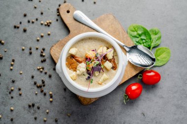 Bir kase kremalı mantar çorbası, yanında da kızarmış ekmek ve şifalı ot. Genel bir bakış, dilimlenmiş mantarlar, kıtır ekmekler ve ahşap bir tahtanın üzerinde taze otlarla süslenmiş beyaz bir kase kremalı mantar çorbası yakalar..