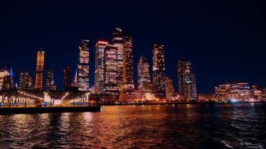 New York, ABD, 6 Aralık 2025: New York 'taki yüksek binalar gece gökyüzünü aydınlatıyor. Onların parlak ışıkları suyu yansıtır. Liman meşgul, akşam boyunca şehrin faaliyetlerini gösteriyor..