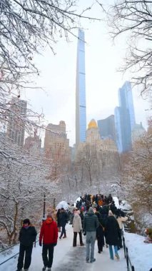 New York, ABD, 24 Aralık 2025: Gökdelenli Karlı Central Park Yolu. Manhattan gökdelenlerine doğru giden karlı Central Park geçidi canlı bir kış şehri yaşam tarzı yaratıyor..