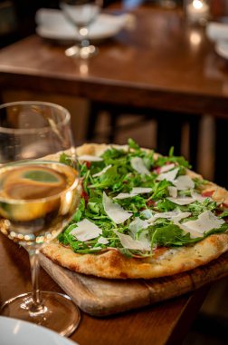 Sıcak bir restoranda beyaz şarapla servis edilen lezzetli pizza. Sebze ve peynirle kaplı bir tabak pizza bir restoranda bir bardak beyaz şarabın yanında oturur..