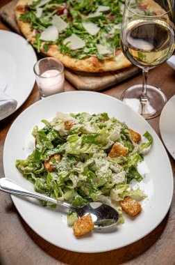 Restoran masasında taze salata, kızarmış ekmek ve bir bardak şarap. Bir kase salata, marul, kızarmış ekmek ve peynirli pizza ve ahşap masada bir içki..