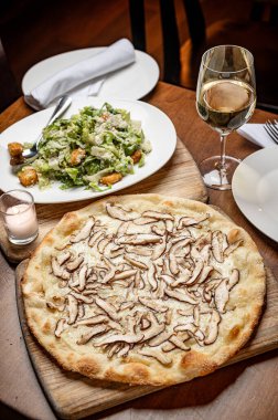 Akşam yemeği tabağında mantar ve salata var. Mantarlı yuvarlak bir pizza bir salata ve bir restoran masasında beyaz şarapla servis edilir..