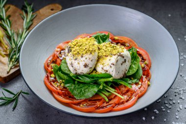 Salad with tomatoes, spinach, and cheese served in a bowl on a table. A bowl holds a salad with fresh tomatoes, spinach, cheese, and nuts on a wooden table.
