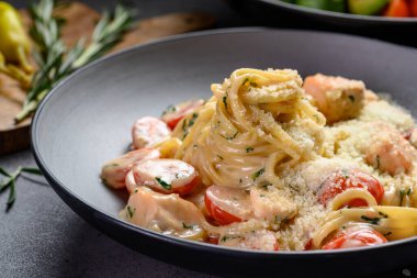 Soslu ve sebzeli makarna tabağı koyu bir kasede servis edilir. Bu makarna tabağında soslu spagetti ve vişneli domates var. Malzemeler bir kasede karıştırılır..