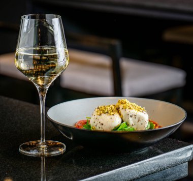 Restoran masasında taze salata, peynir ve beyaz şarap. Restoranda bir kase peynirli ve fındıklı salatanın yanında bir bardak beyaz şarap duruyor..