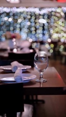 Arka planda ışık dizeleri olan bir restoranda akşam yemeği. Arka planda süslemeler ve ışıklar olan bir restoranda akşam yemeği için masalar ayarlandı..