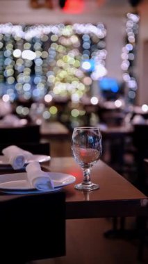 Lokantadaki misafirler için akşam yemeği, cam ve tabaklar hazır. Bir masa beyaz tabaklar ve bir bardakla hazırlandı. Lokantanın arka planında hafif ışıklar parlıyor..