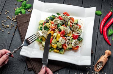 Tabakta taze sebze salatası ve ahşap bir masada çatal bıçak. Bir insan, yanında çatal bıçak takımı olan kare bir tabakta karışık sebze yemek üzere..