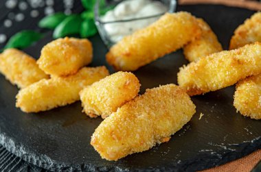 Siyah bir tabakta kızartılmış atıştırmalıklar soslu ve arka planda otlar. Kızarmış abur cuburlar siyah bir tabakta yanında küçük bir kase sos, arka planda otlar..