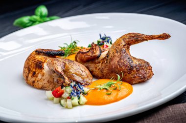 Beyaz tabakta sebze salatasıyla servis edilen ızgara bıldırcın. Izgara bıldırcın, renkli salata ve sosla birlikte beyaz bir tabağa konur. Yemek hazır görünüyor..