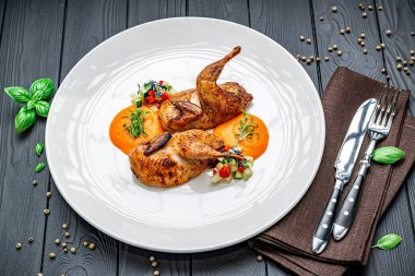 Beyaz tabakta renkli sebze salatasıyla servis edilen ızgara bıldırcın. Bıldırcın ızgara yapılır ve yanında renkli salata ve sos ile beyaz bir tabağa yerleştirilir..