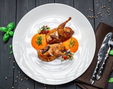 Öğle yemeği için soslu ve taze sebzeli ızgara bıldırcın servis ediliyor. İki ızgara bıldırcın soslu ve etraflarında doğranmış sebzelerle beyaz bir tabağa konur..