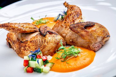 Restoran ortamında sebze garnitür ve sosla servis edilen ızgara tavuk. Izgara tavuk, soslu ve sebze parçalı beyaz bir tabağa konur..