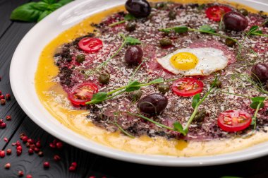 Yumurta, zeytin, vişneli domates ve baharatlı Carpaccio tabağı. Bir tabak, üzerinde yumurta, zeytin, domates ve yemeye hazır bitkiler bulunan carpaccio tutar..