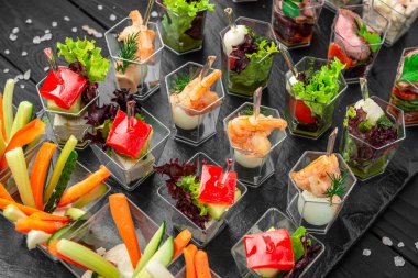 Açık büfede karides, sebze ve garnitürlü çeşitli küçük tabaklar. Konuklar bir etkinlikte karides, sebze ve taze sebzelerin yer aldığı veya toplandığı küçük tabakları beğeniyorlar.