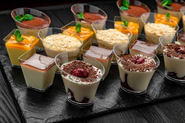 Çeşitli tat ve dokulara sahip bir toplantıda siyah bir tabakta tatlılar. Tatlılar siyah bir tabakta sergilenir. Üzerinde farklı aromalar ve süslemeler bulunur..