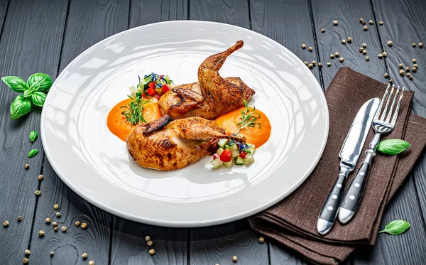 Beyaz tabakta taze sebze ve sos ile servis edilen bıldırcın. Bıldırcın, doğranmış sebzeler ve ahşap bir masada otların yanında sosla dolu bir tabakta..