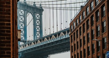Brooklyn 'deki caddeden Manhattan Köprüsü' nün her iki tarafında binalar var. Manzara, Brooklyn 'de puslu bir günde tuğla binaların çerçevelediği Manhattan Köprüsü' nü gösteriyor..