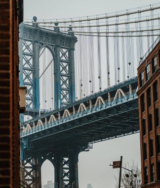 Şehirdeki caddeden Manhattan Köprüsü 'nün manzarası. İnsanlar bulutlu bir günde Manhattan Köprüsü 'nü izlerken binaların yanında yürürler..