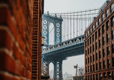 Dar bir sokaktan Manhattan Köprüsü 'nün yanında tuğla binalar var. Bir insan dar bir sokakta durup Manhattan Köprüsü 'ne bakar..